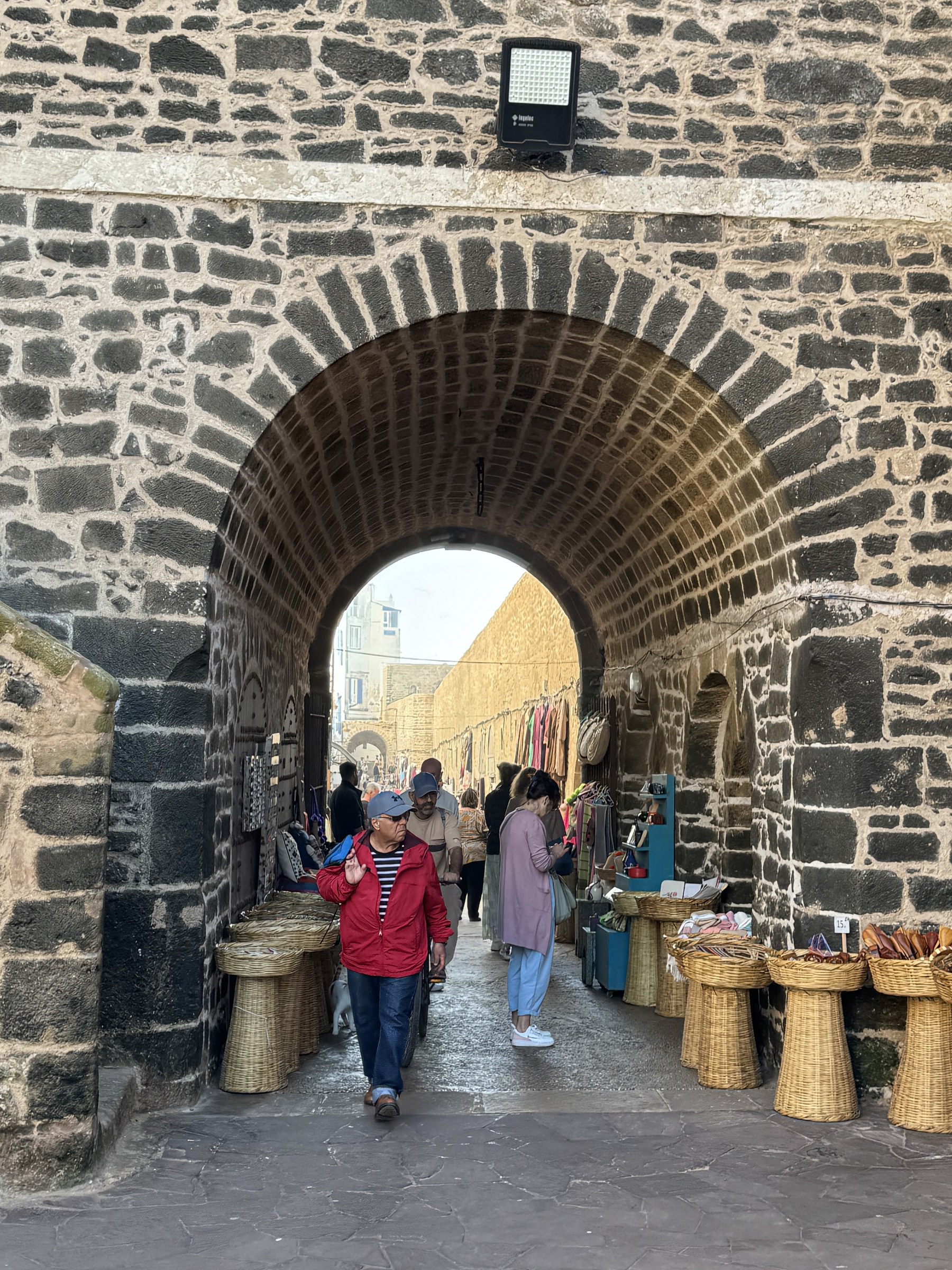 Arco de piedra en la muralla de Essaouira con puestos de artesan&iacute;a y turistas paseando