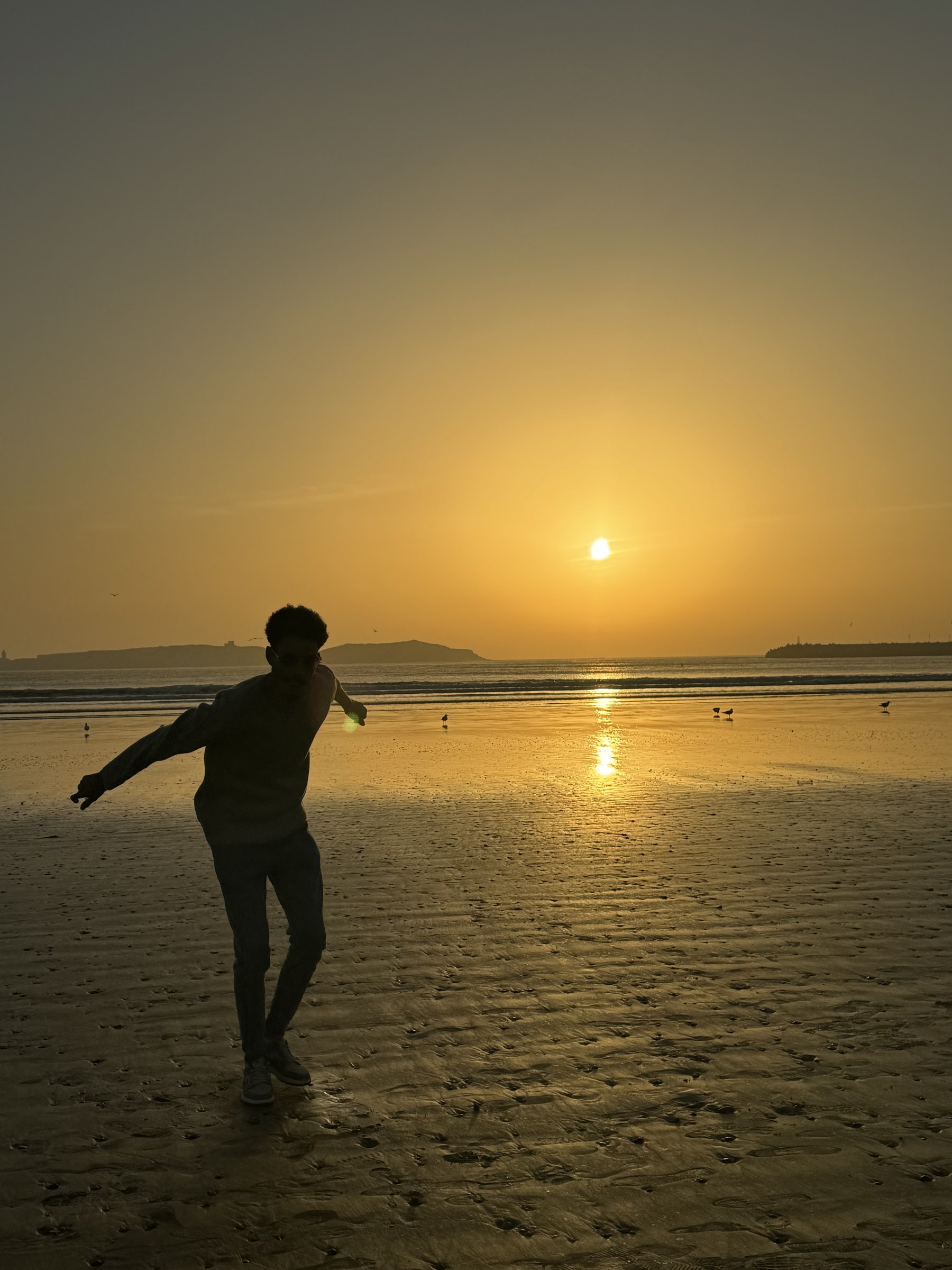Silueta de persona bailando en la playa de Essaouira al atardecer con el sol dorado