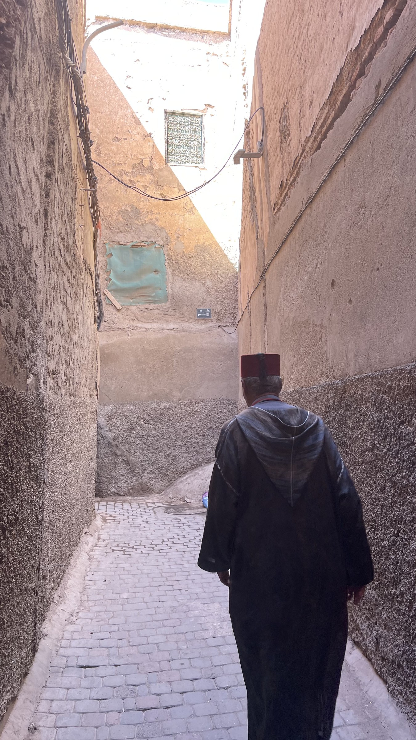Hombre con djellaba y fez rojo camina por callejón estrecho de la medina de Marrakech