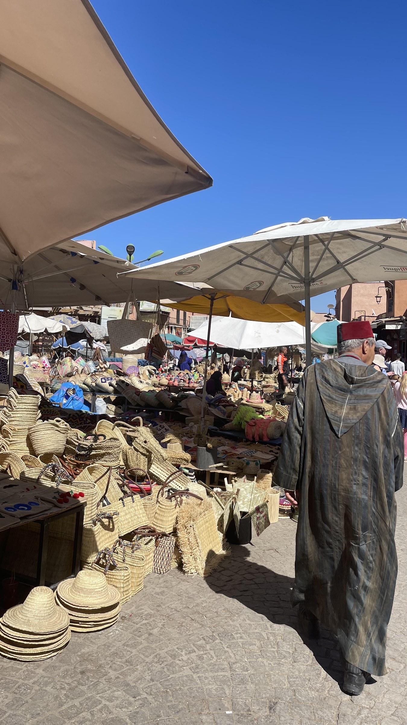 Mercado al aire libre en Marrakech con cestas de esparto y hombre en djellaba y fez rojo entre comercios