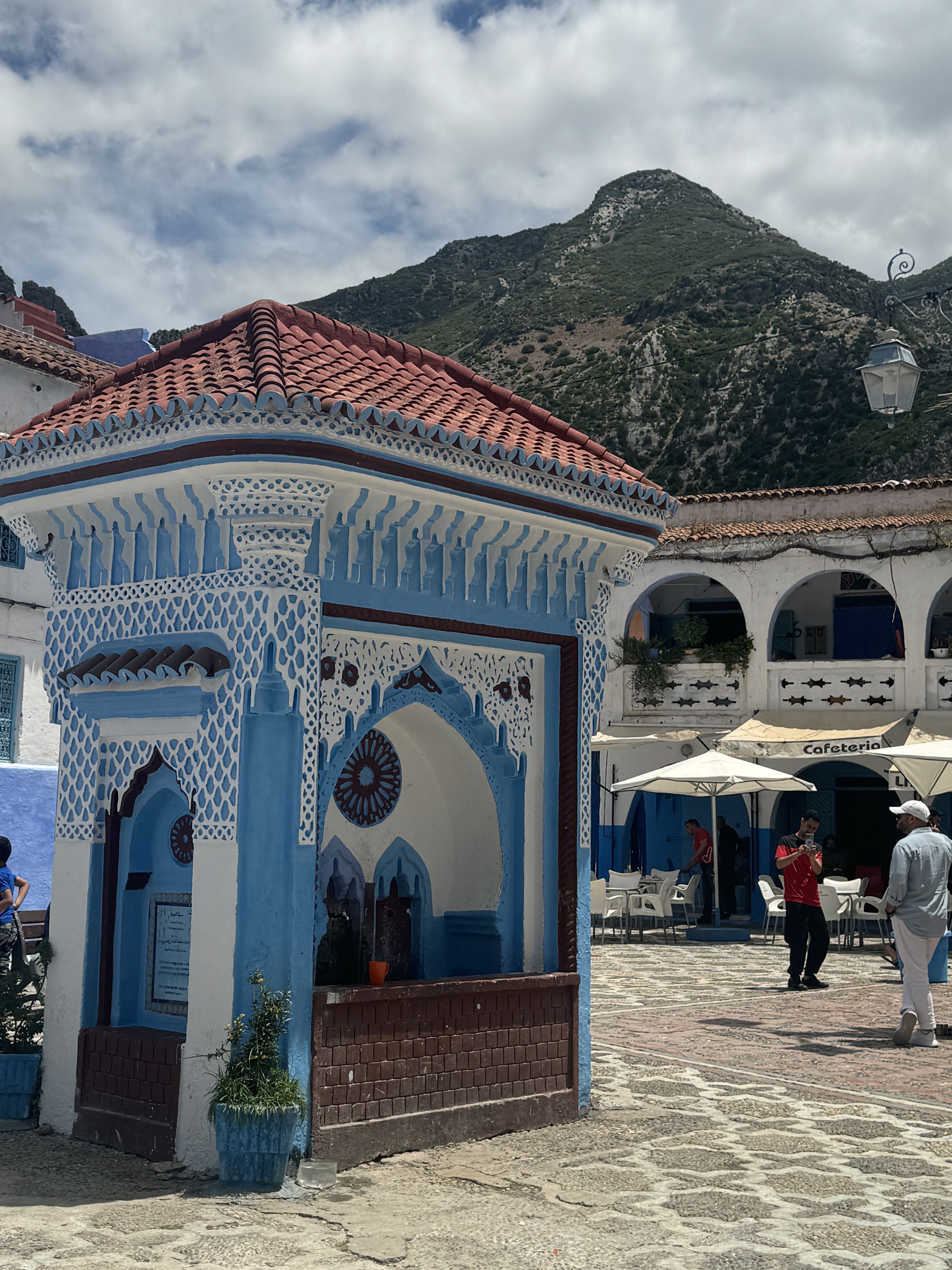 Plaza Uta el-Hammam de Chefchaouen con fuente octogonal azul y blanca y montañas del Rif al fondo