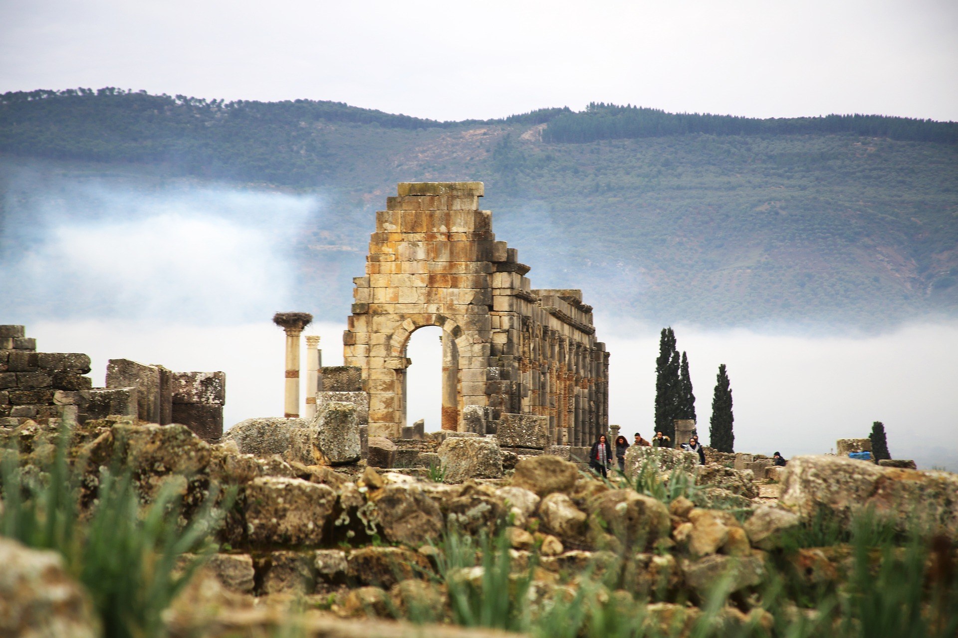 Ruinas romanas de Volubilis con arco y columnas entre niebla y monta&ntilde;as verdes, Patrimonio UNESCO en Marruecos