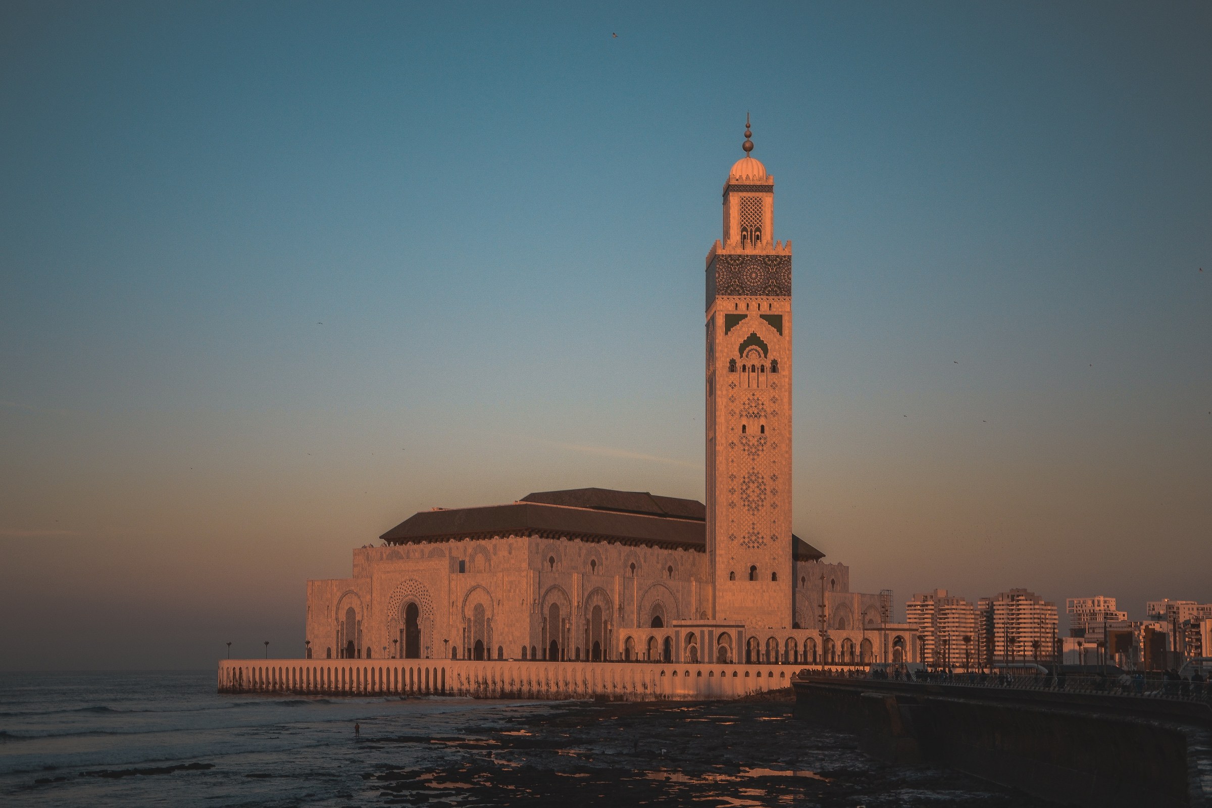 Mezquita Hassan II de Casablanca al atardecer con su minarete iluminado sobre el océano Atlántico
